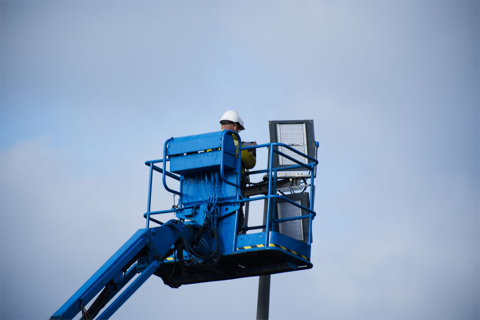 Helmeted electrical worker servicing an LED streetlight from an aerial lift